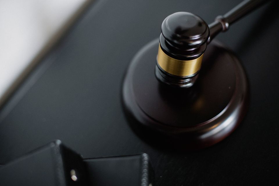 Nahaufnahme eines Richterhammers auf einem Holztisch vor dem Hintergrund einer Justitia-Figur.